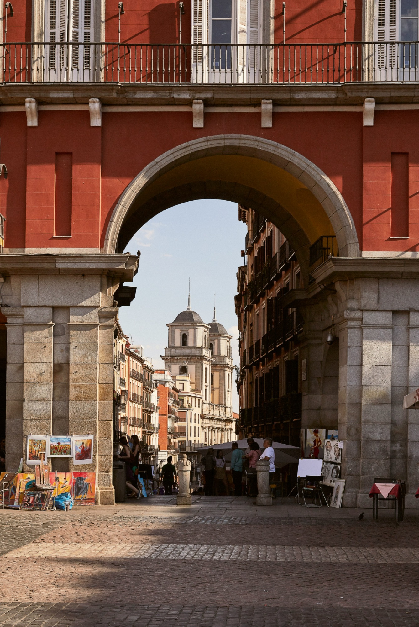 The stone arch of Plaza Mayor framing a Centro street and church towers beyond