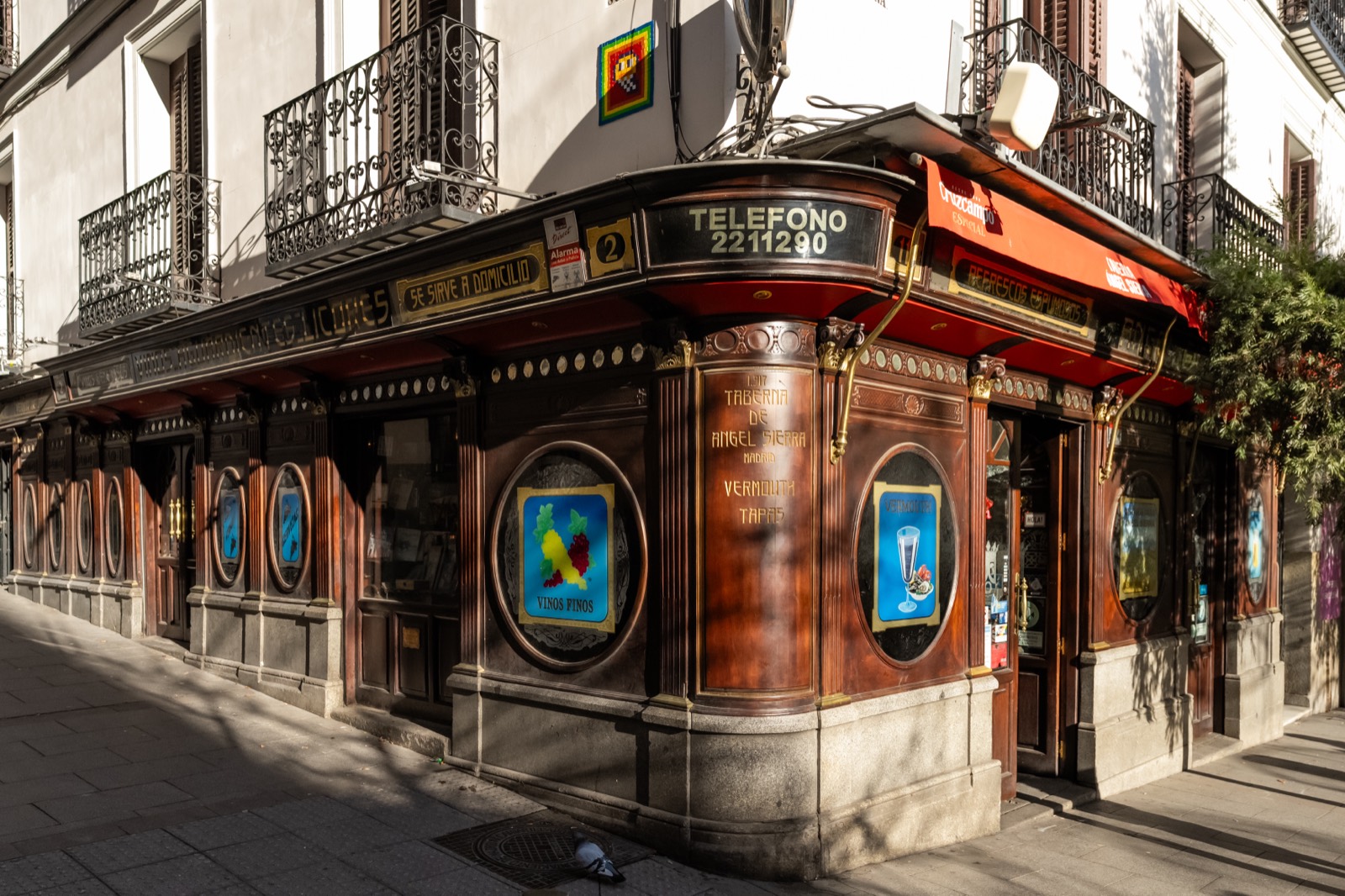 The carved wood and brass corner façade of Taberna de Ángel Sierra in Chueca, its 1917 vermouth and tapas signage lit by low sun