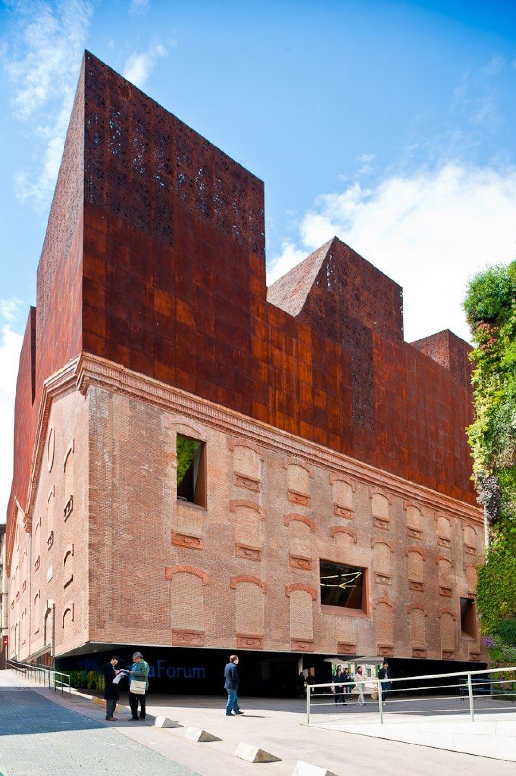 The rusted corten-steel and brick form of CaixaForum Madrid rising beside its vertical garden under a blue sky