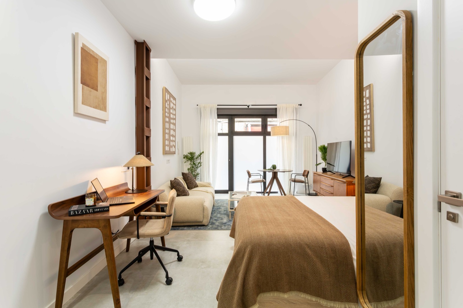 A bright, warm-toned Akora studio apartment in Madrid with a wooden desk and laptop, sofa and doors to a patio