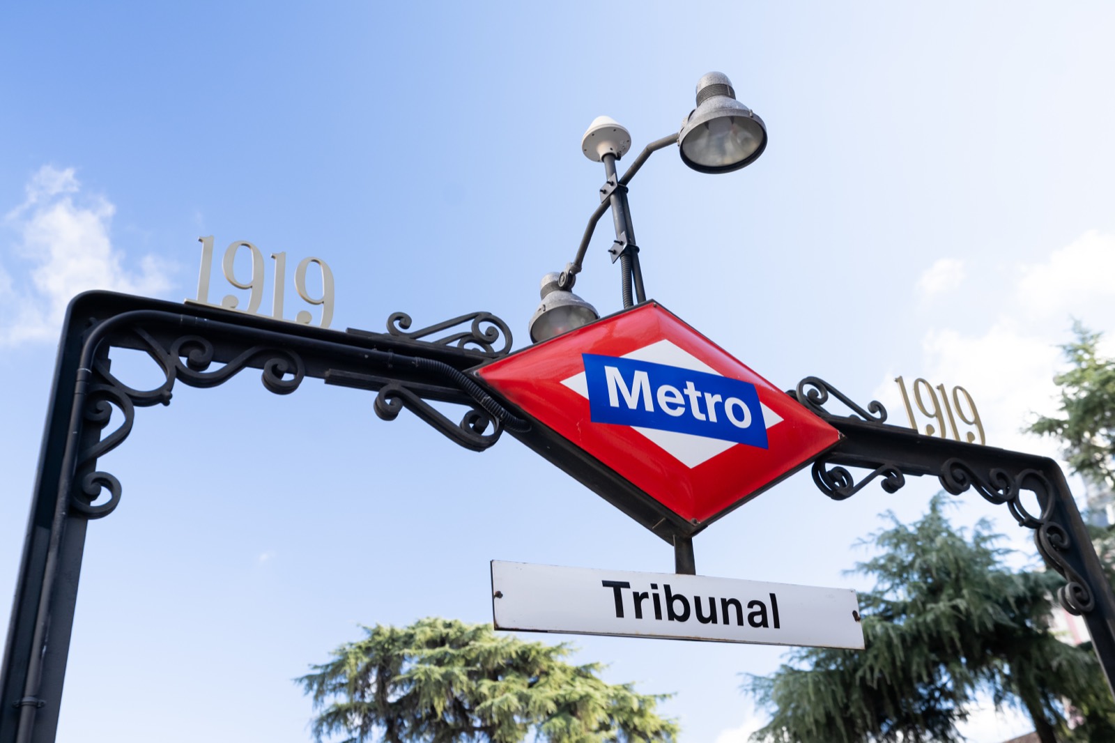 The wrought-iron Metro sign at Tribunal station in Madrid, marked 1919, against a blue sky