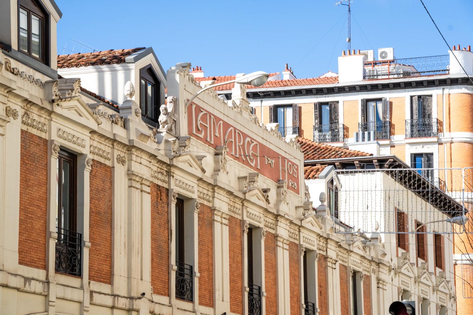 Sunlit brick and stone façades of classic Madrid apartment buildings against a deep blue August sky