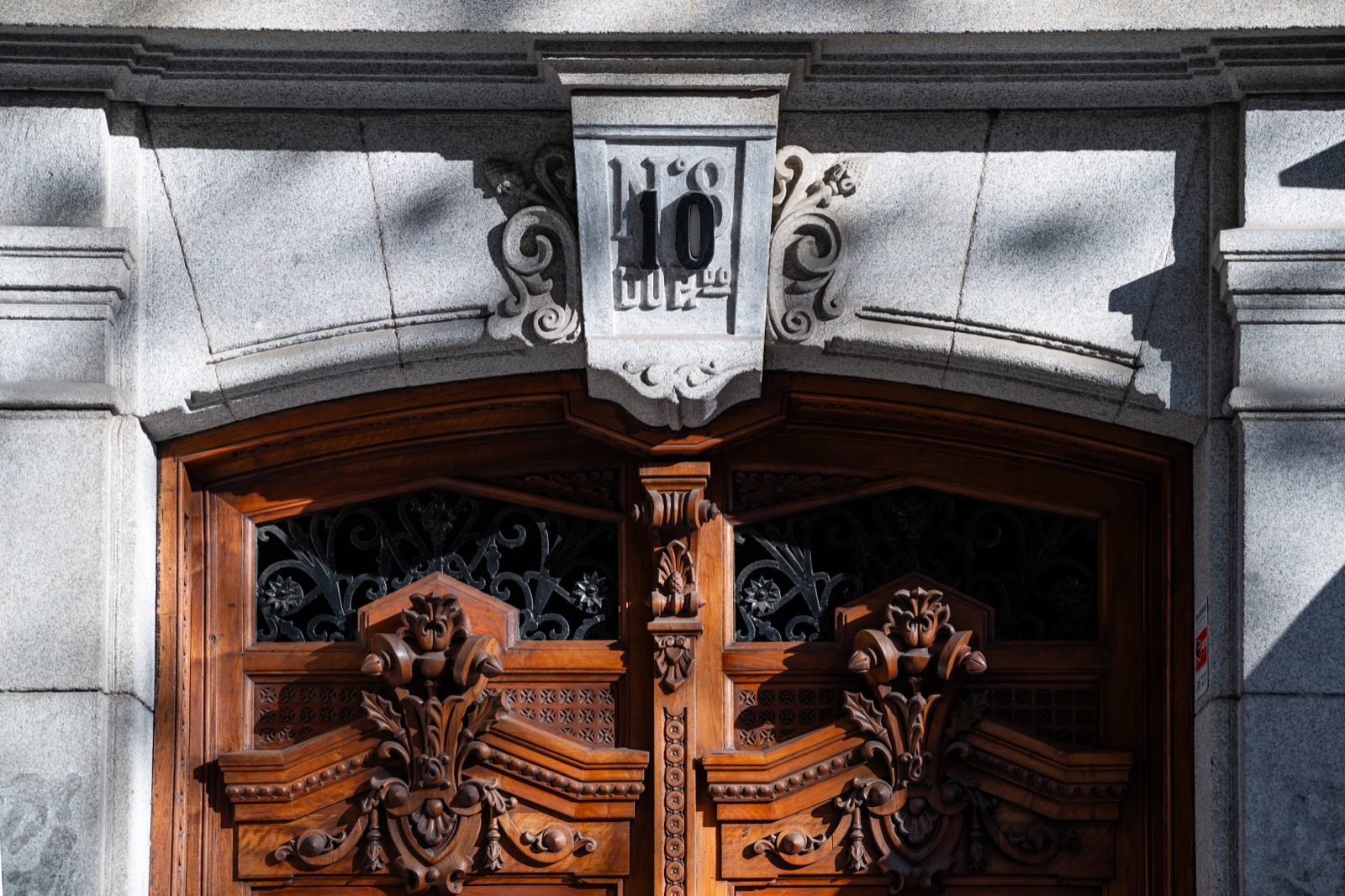 An ornate carved wood and wrought-iron doorway beneath a stone number 10 on a classic Madrid apartment building