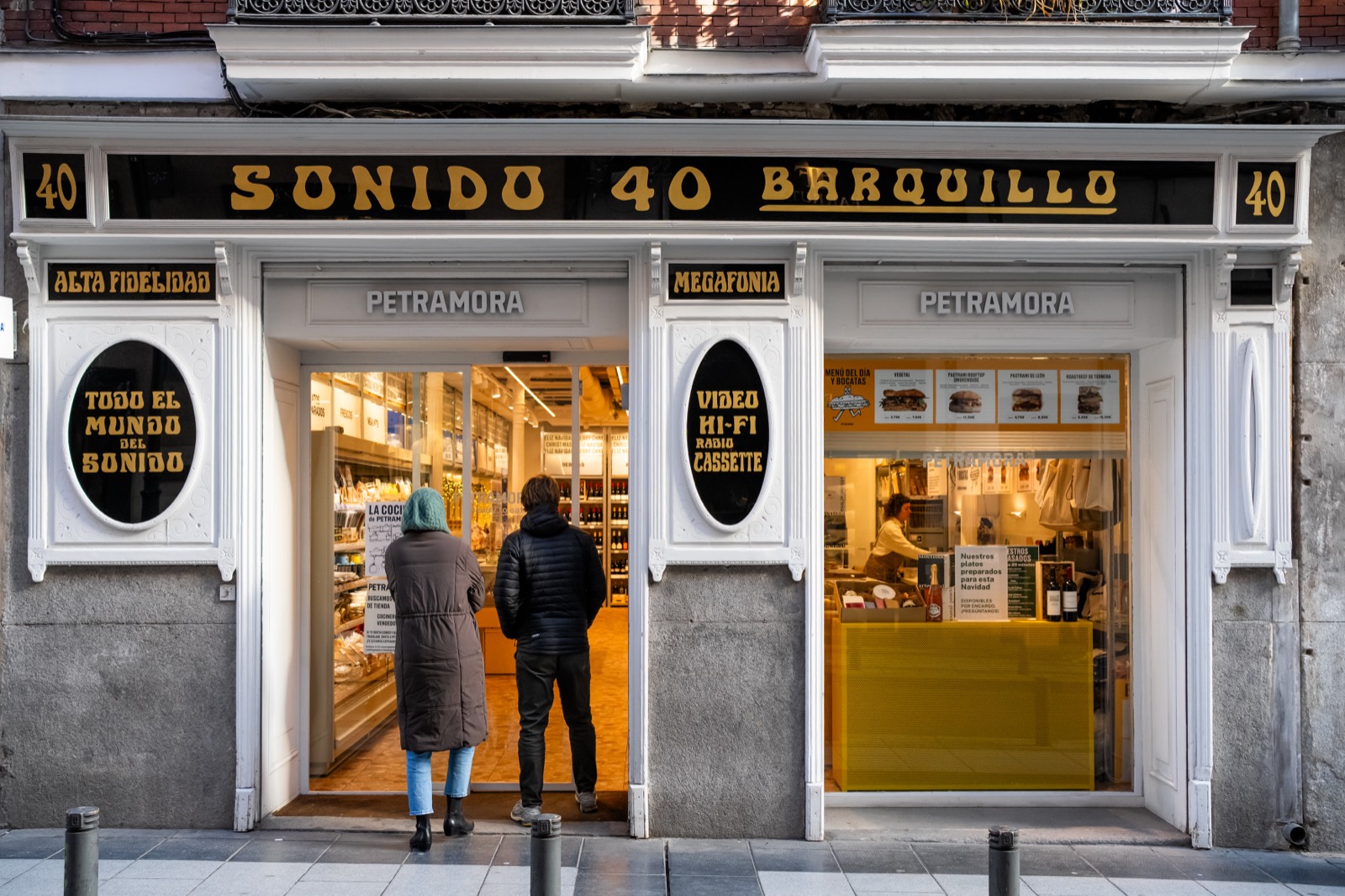 Two people at the counter of Petramora, a gourmet shop and bar on Calle Barquillo in Chueca, Madrid
